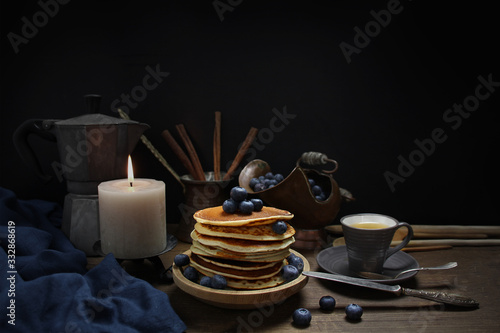 national dish pancakes, pancakes, pita with blueberries, linen napkin, a candle burns, a cup of tea, an old mocha coffee machine, a concept of traditional cuisine