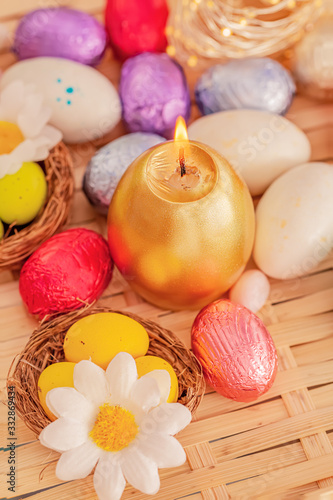 Festive easter concept of candle and colorful eggs on a wooden table. Daisy  flower, green eggs in the nest. Greeting card Easter.