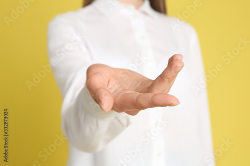 Young woman against yellow background, focus on hand