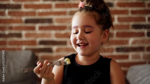 People and food: A little girl is eating spaghetti pasta with nuggets and tomato at the table in the room with a fork . Portrait of a kid eats with appetite at home in front of the camera
