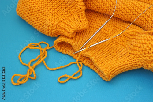 Knitting wool sweater and knitting needles on blue background, copy space