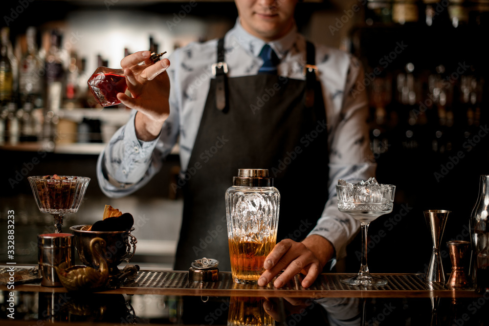 young barman adds ingredient for cocktail to glass shaker.