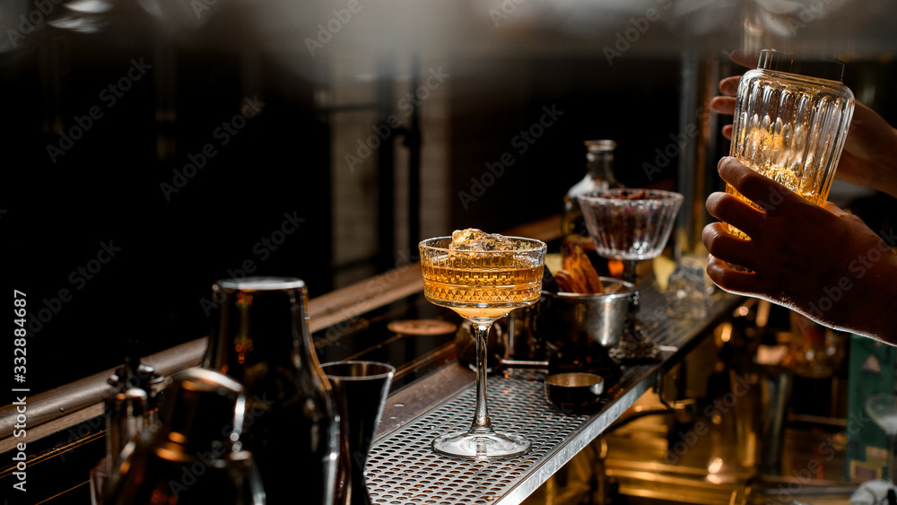 glass of ice brown alcoholic drink stands on bar counter.