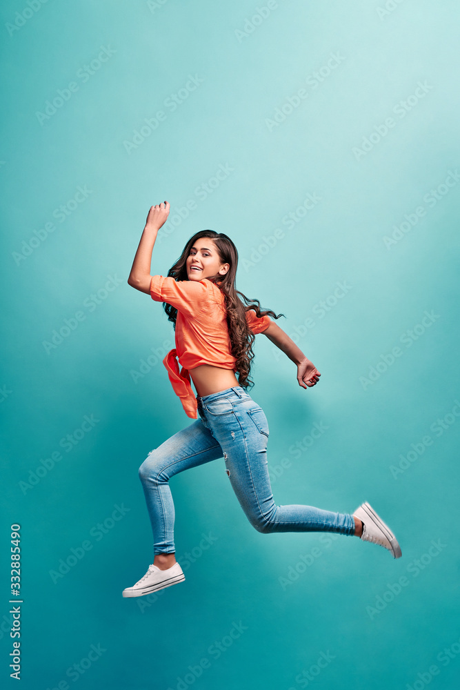 Beautiful young attractive careless girl jumping having fun fooling flying isolated on bright vivid turquoise color background. Concept of carefree and cheerful mood.Full length body size view.