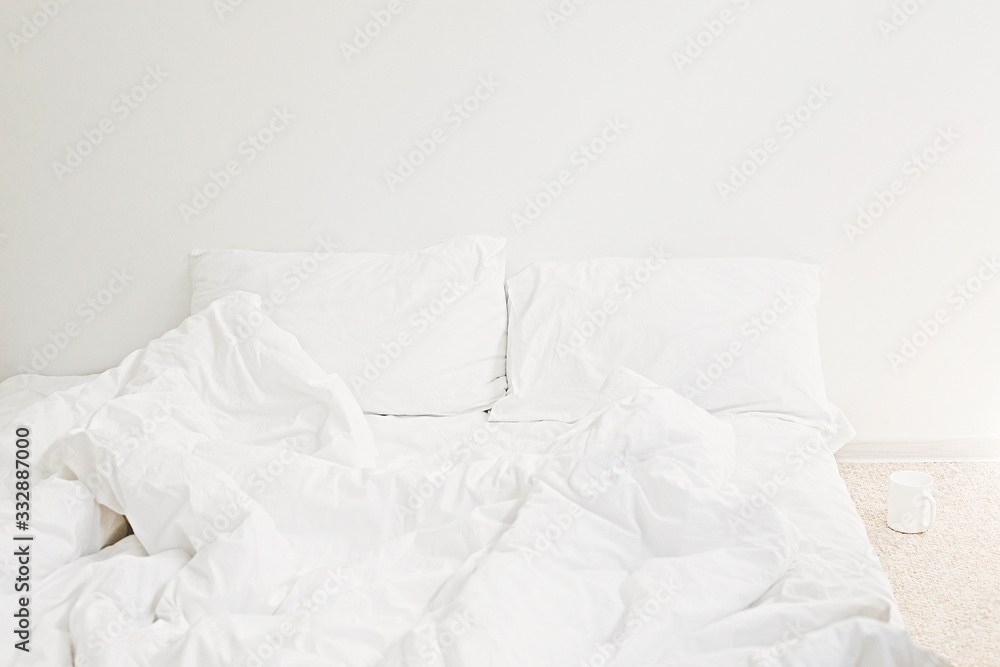 Cozy white bed in the morning. White sheets and pillow on bed in modern white room. Lazy days. Stay home. Comfortable place. Relax on weekend in hotel room. Messy bed