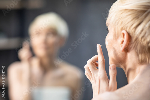 Lady Applying Face Cream Standing Back To Camera In Bathroom