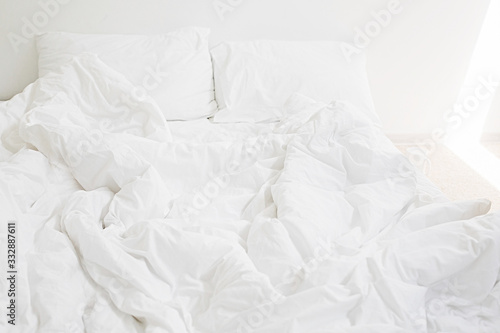 Cozy white bed in the morning. White sheets and pillow on bed in modern white room. Lazy days. Stay home. Comfortable place. Relax on weekend in hotel room. Messy bed