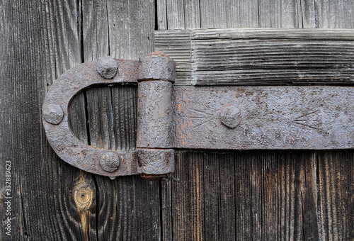 An old iron door hinge covered in rust hangs from an old wooden gate