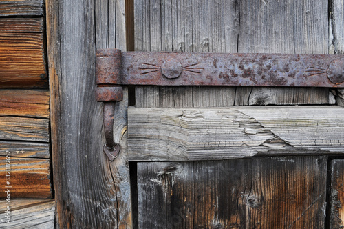 An old iron door hinge covered in rust hangs from an old wooden gate
