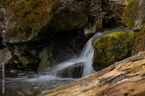 A beautiful small waterfall in a thicket of forest on high hills among huge boulders covered with moss