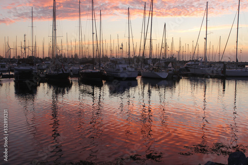  the evening sun casts a red glow on the water in the harbor where the sailing boats are moored