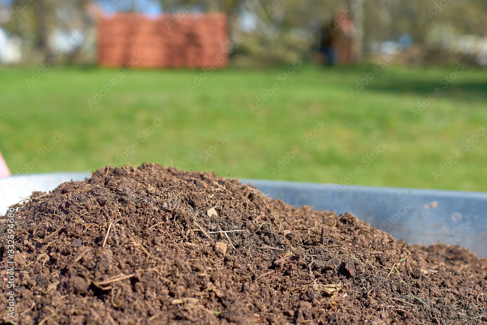 Fototapeta premium Fresh compost in a wheelbarrow with a green meadow in the background
