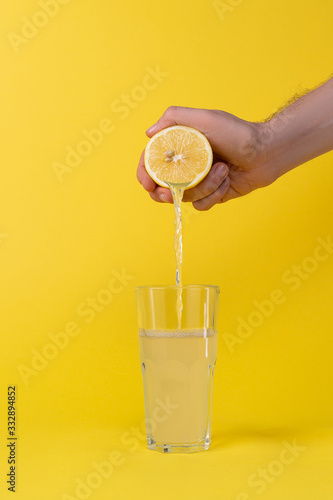 Фотография squeezing lemon juice into glass on yellow background