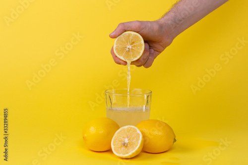 squeezing lemon juice into glass on yellow background