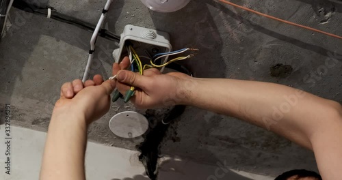 Male electrician manually twists electrical wires in junction box, puts on an insulating rubber black cap, does not use tools, replacing wiring, major repairs of room, energy, electrical work