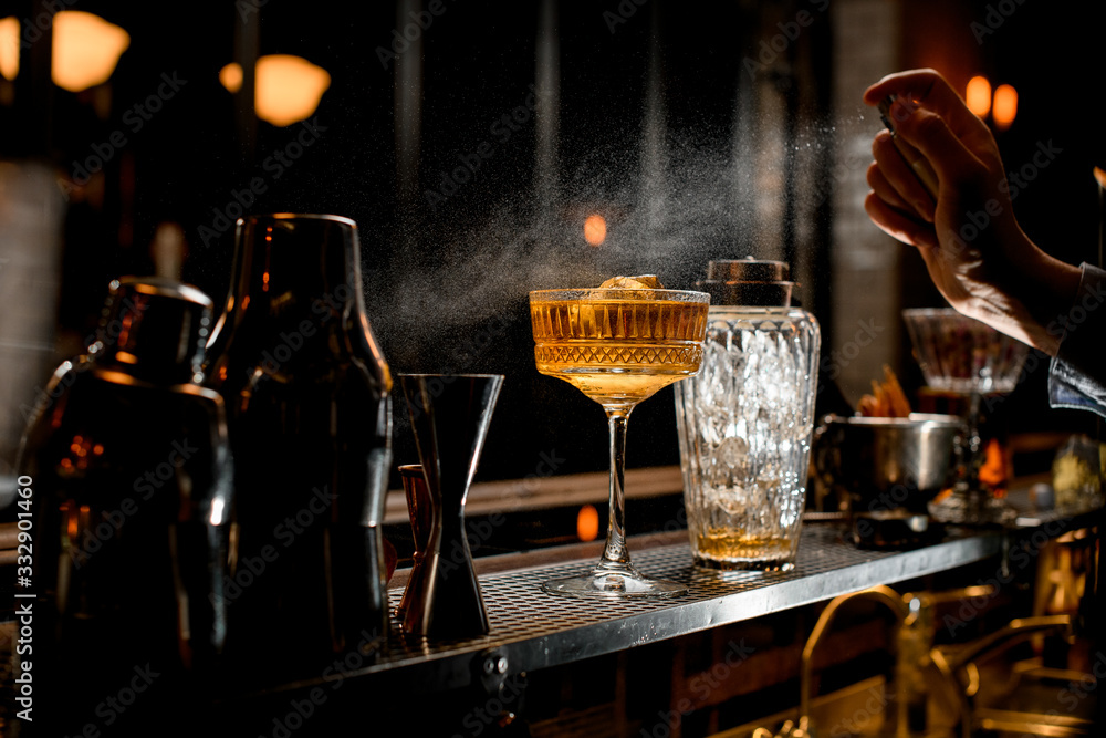 Bartender's hand sprinkles on glass with brown alcoholic cocktail.