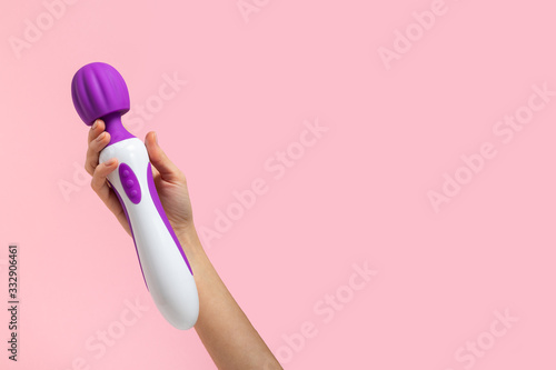 Girl's hand holds a pink massager for sex. Vibrator for masturbation. Dildo for vaginal and clitoral stimulation. Image for sex shop. Sex toys for adults. Massager for the clitoris.
