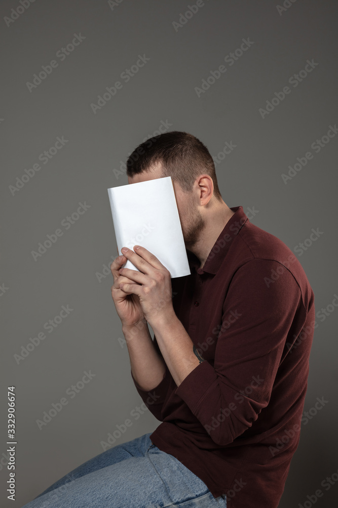 Happy world book and copyright day, read to become someone else - man covering face with book while reading on grey studio background. Celebrating, education, art, enjoying new characters concept. Happy world book and copyright day, read to become someone else - man covering face with book while reading on grey studio background. Celebrating, education, art, enjoying new characters concept.