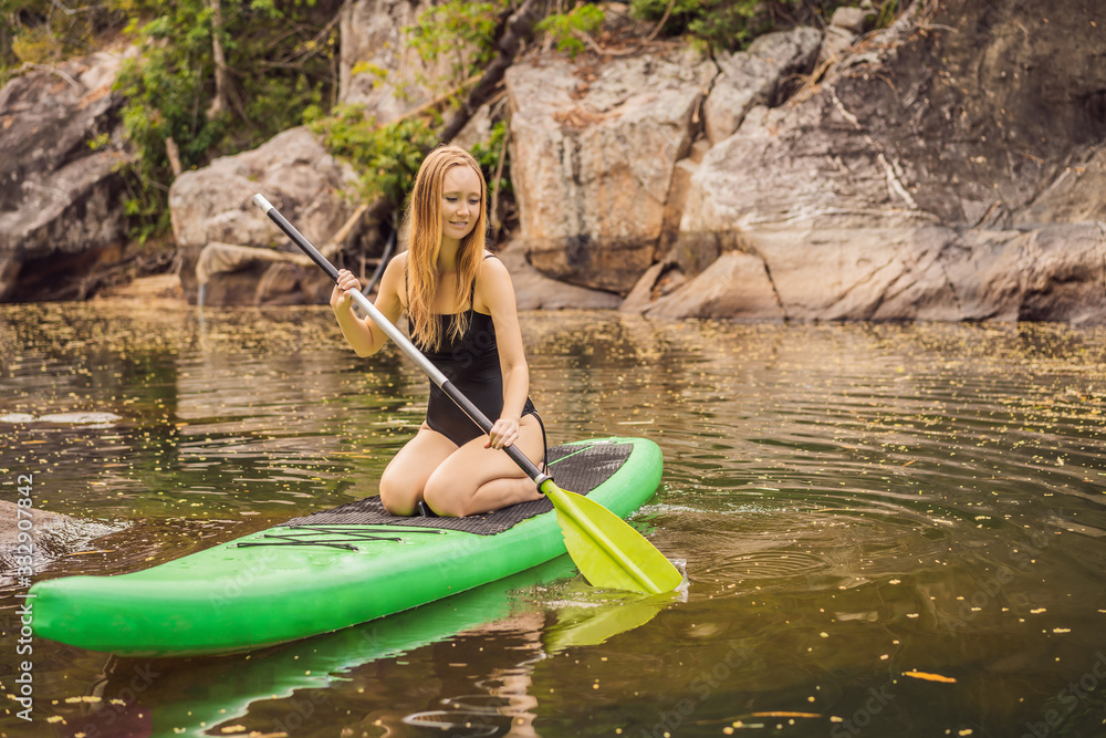 SUP Stand up paddle board woman paddle boarding on lake standing happy on paddleboard on blue water. Action Shot of Young Woman on Paddle Board SUP Stand up paddle board woman paddle boarding on lake standing happy on paddleboard on blue water. Action Shot of Young Woman on Paddle Board