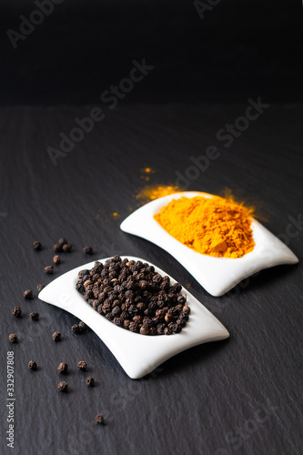Healthy food and alternative medicine ingredient concept organic Black peppers and turmeric powder in square ceramic cup on black slate stone board with copy space.