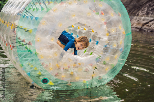 Cute little boy, playing in Zorb a rolling plastic cylinder ring with a hole in the middle on the lake photo