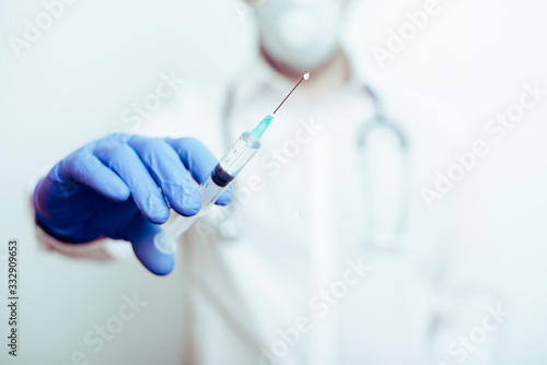 detalle de una jeringuilla en una mano con guante azul de un doctor con fondo desenfocado