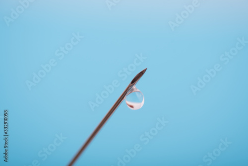 detalle de una gota saliendo de la aguja de una jeringuilla sobre fondo azul liso con espacio