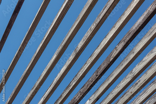 Oblique view of weathered wood beams against a blue sky, abstract background pattern, horizontal aspect