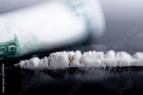 white powder (heroin, cocaine, narcotic) scattered in the form of a track, a bill folded into a tube lies side by side, shot very close up with a soft focus