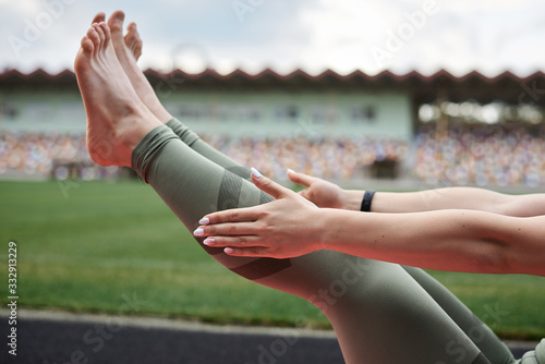 Close-up picture of legs and arms in process of doing abs.Sportswoman, wearing green leggings, doing abs on city stadium, Power fitness training outside on pink yoga mat. Healthy active life concept.