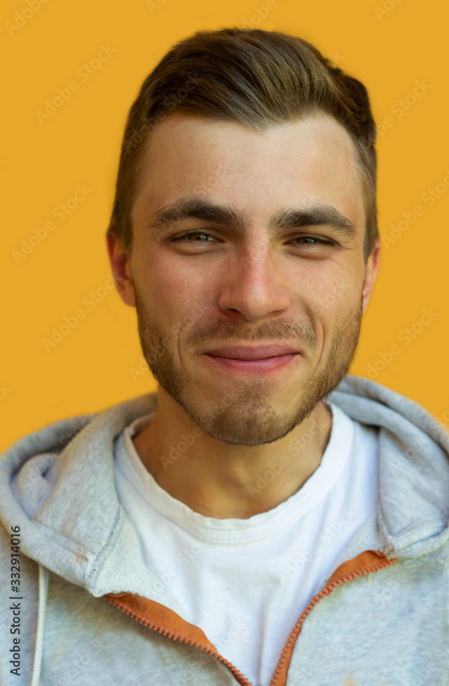 Fototapeta premium young hipster with a beard smiles and looks at the camera on a background of a yellow wall.
