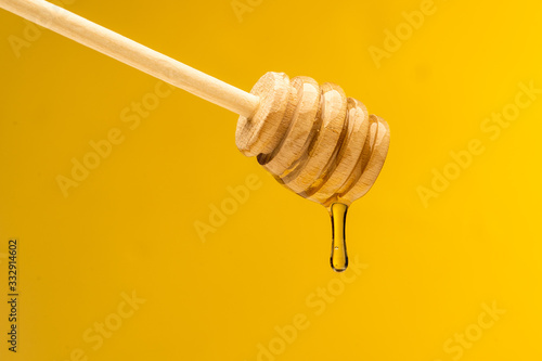 dripping sweet honey from wooden dipper on yellow background