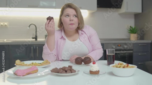 Young fatty woman hiccupping while eating sweet dessert at home, sugar overdose photo