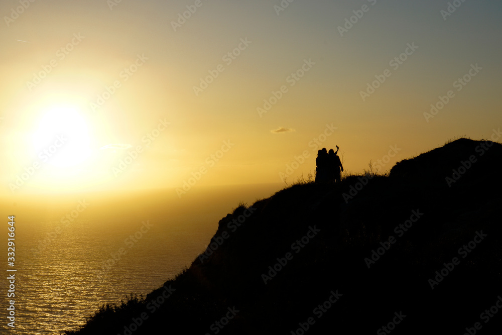  A group of people taking a selfie during sunset on their holiday by the cliff in Malta
