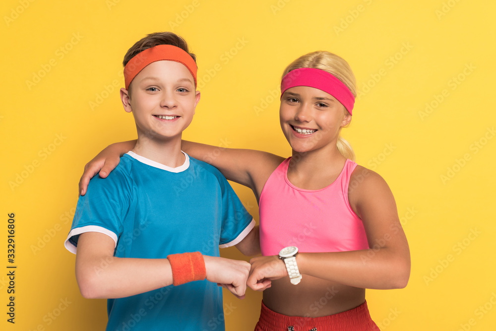 smiling kids in sportswear hugging and doing fist bump on yellow background smiling kids in sportswear hugging and doing fist bump on yellow background