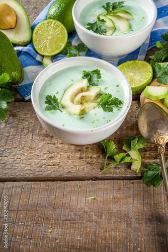 Homemade avocado cream soup with lime, herbs and avocado slices on wooden rustic background, copy space