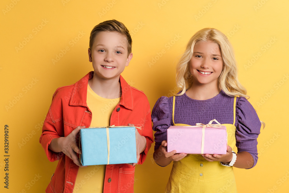 smiling friends holding gift boxes on yellow background smiling friends holding gift boxes on yellow background