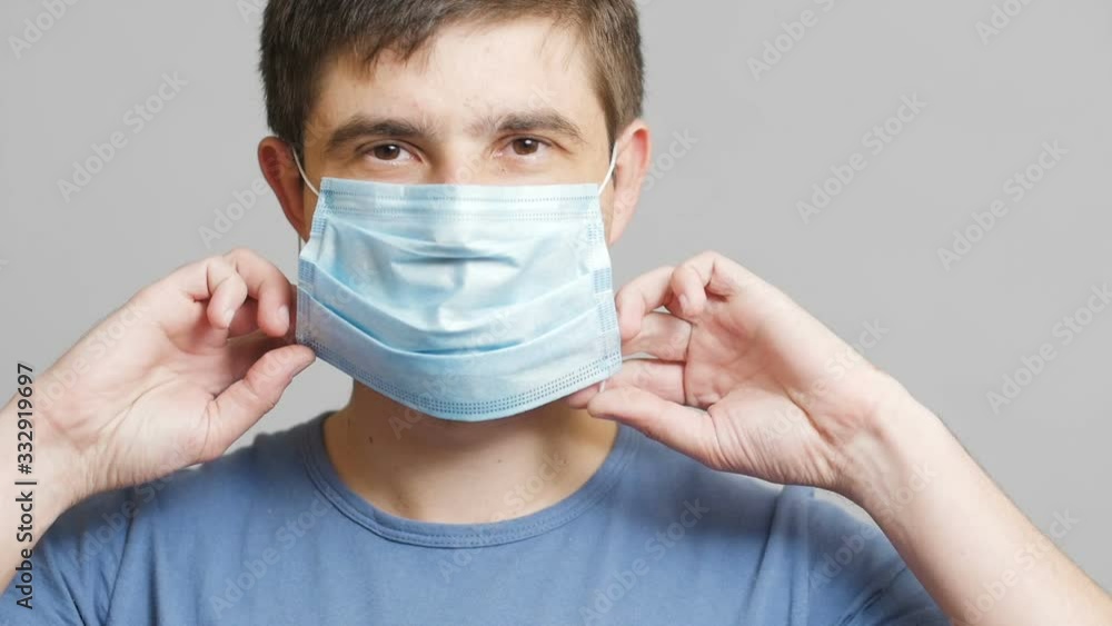 face of a young doctor putting on surgical mask on mouth on a gray studio background, concept of medicine and health, quarantine measures face of a young doctor putting on surgical mask on mouth on a gray studio background, concept of medicine and health, quarantine measures
