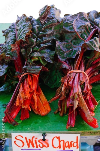 Bunches of rainbow Swiss chard with bright red and orange stalks and green leaves for sale at a farmers market