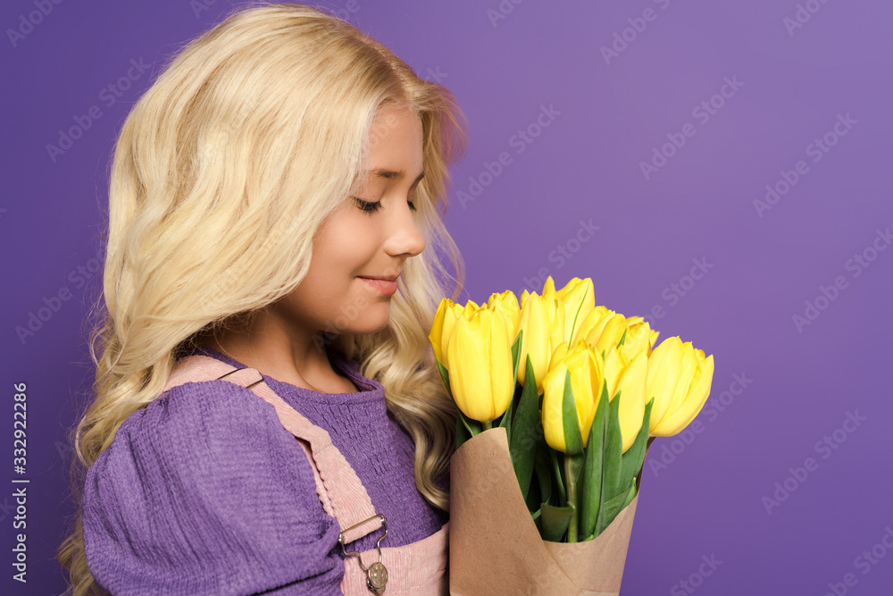 side view of smiling kid holding bouquet of tulips on purple background side view of smiling kid holding bouquet of tulips on purple background