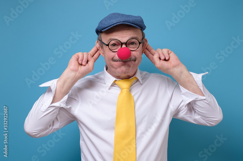 Tableau sur toile Senior caucasian man wearing red nose, hat, and glasses grimacing
