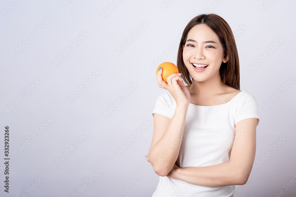 Beautiful young asian holding an orange with big smile in seamless white isolated background. Diet healthy , beauty concept. Beautiful young asian holding an orange with big smile in seamless white isolated background. Diet healthy , beauty concept.