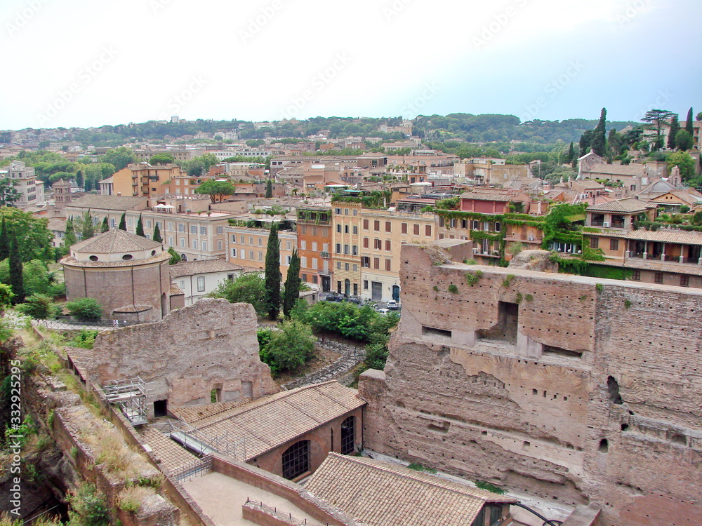 Landscape of millennial columns and dilapidated majestic buildings of mighty Rome in the past, against the backdrop of modern areas under a cloudy sky on the horizon.