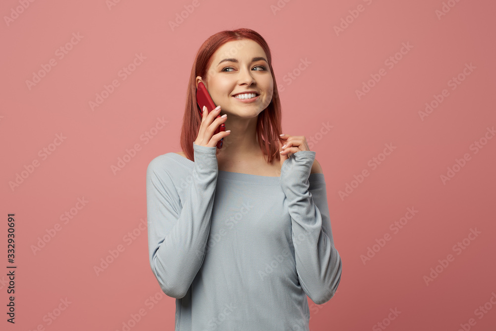 Happy woman talking on phone while standing in studio on pink background Happy woman talking on phone while standing in studio on pink background