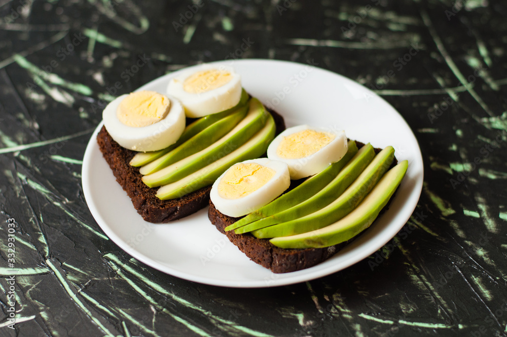 Sandwiches with brown bread, avocado and egg on a dark background, top view Sandwiches with brown bread, avocado and egg on a dark background, top view