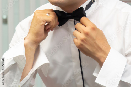 The groom straightens a bow-tie on a shirt close-up