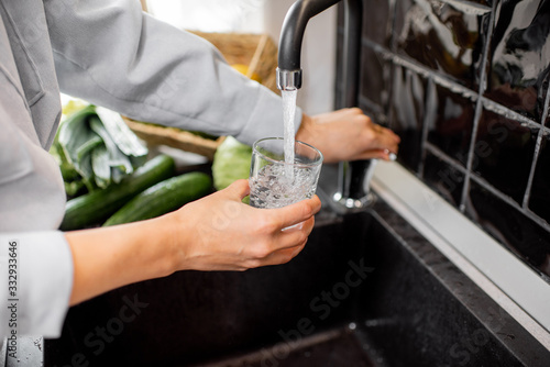 Woman filling drinking glass with tap water on the kitchen. Concept of clean drinking tap water at home