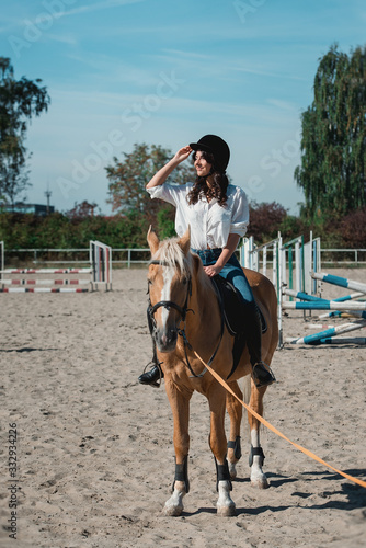 Portrait of young brunette woman in a white shirt and helmet on a horse