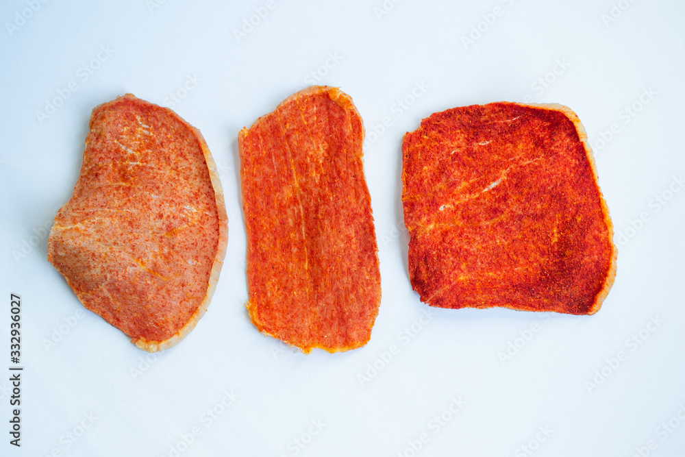 Dried slices of pork, beef of different shapes with spices on a white background. Crispy meat chips. Tasty appetizer. View from above. Dried slices of pork, beef of different shapes with spices on a white background. Crispy meat chips. Tasty appetizer. View from above.