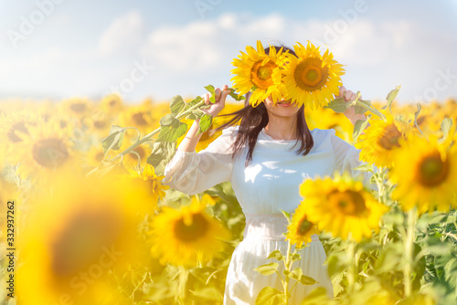 portrait of young and attractive asian woman in beautiful dress standing among full bloom sunflower fields on sunny day with sunflowers hiding her face